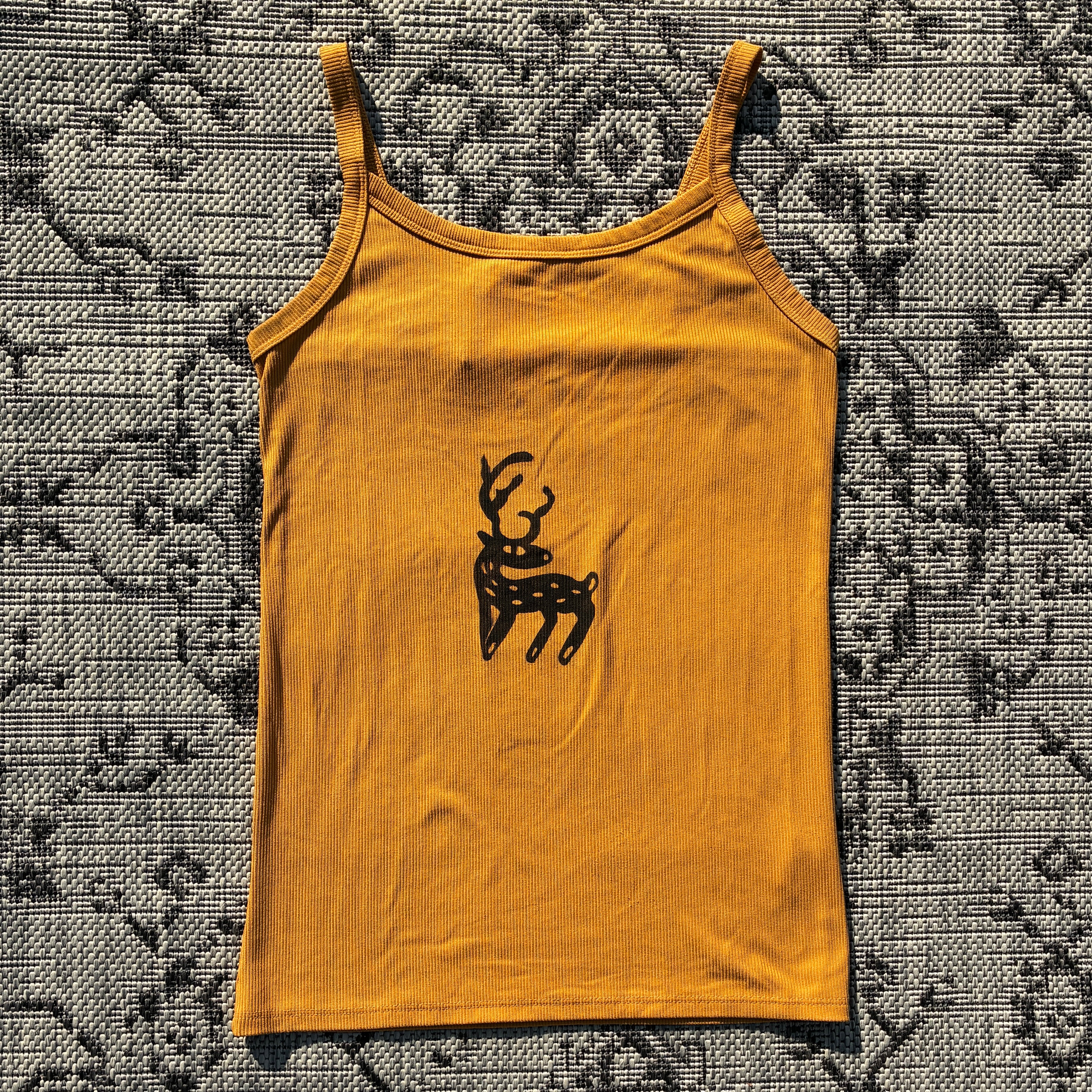 Yellow tank top with a black deer graphic on a patterned fabric background